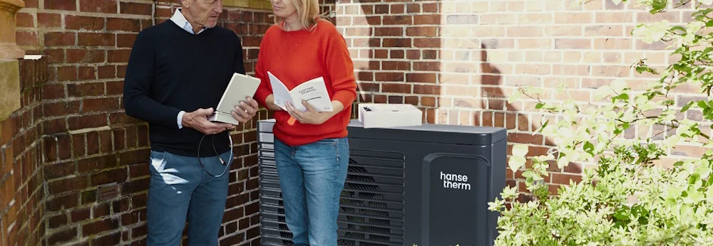 Zwei Personen vor einer Hauswand mit Wärmepumpe